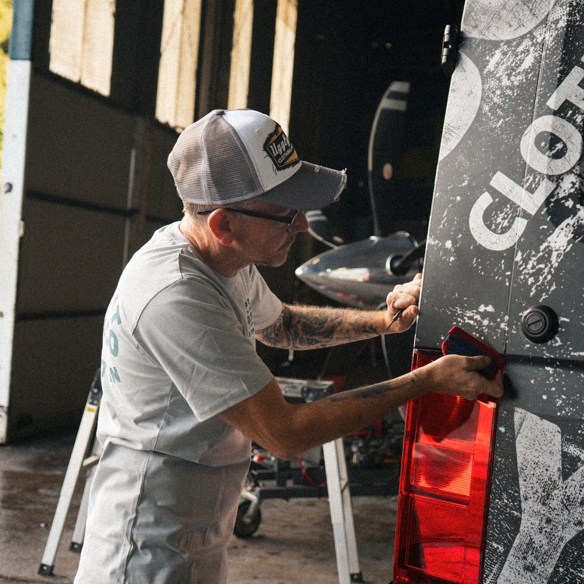 Grey & White Diamond Trucker Cap worn during a van wrapping session inside a hangar.