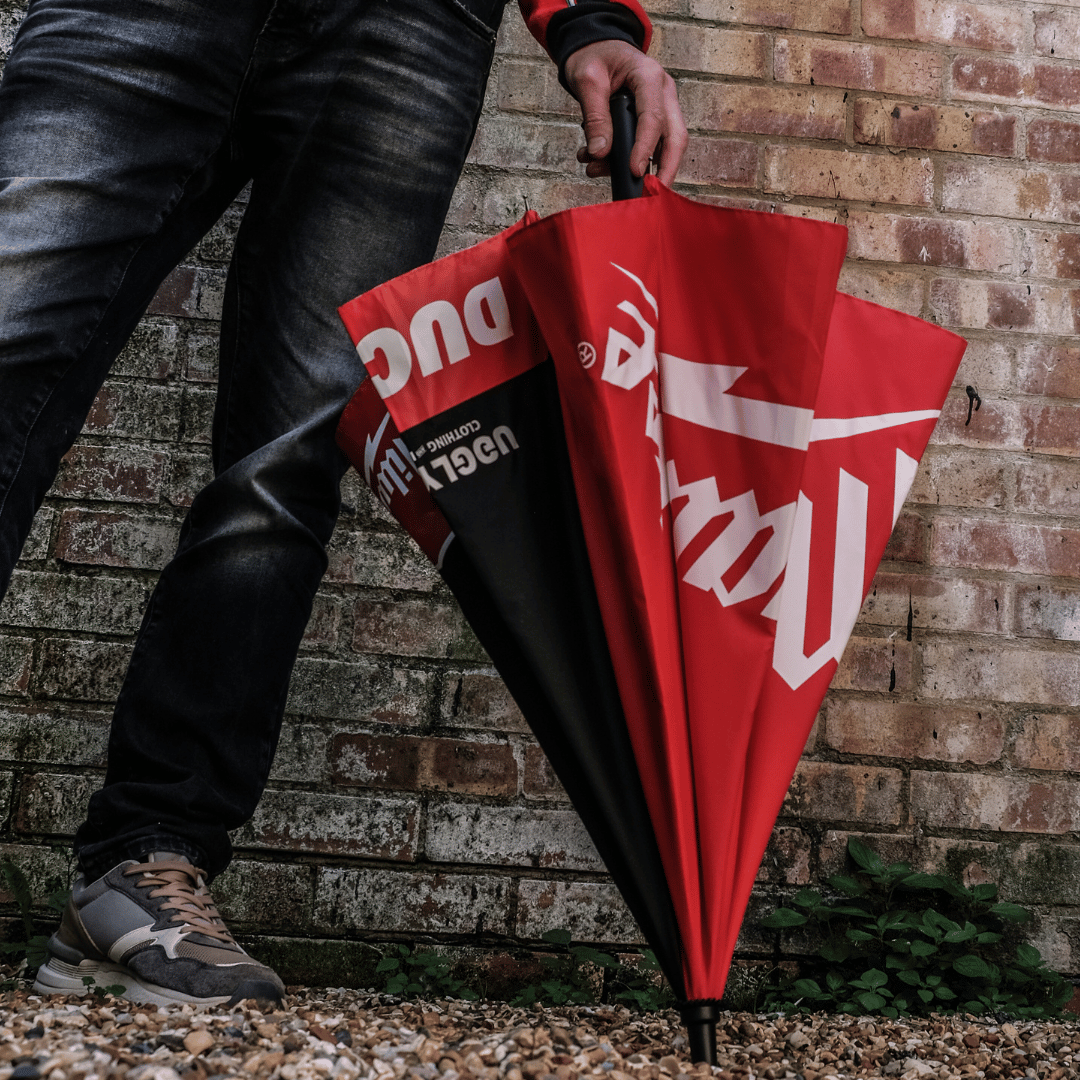 A model holding a Milwaukee Tools x Ducati umbrella with a black canopy and red accents, featuring the Milwaukee Tools logo, Ducati logo, and the Uggly&Co logo