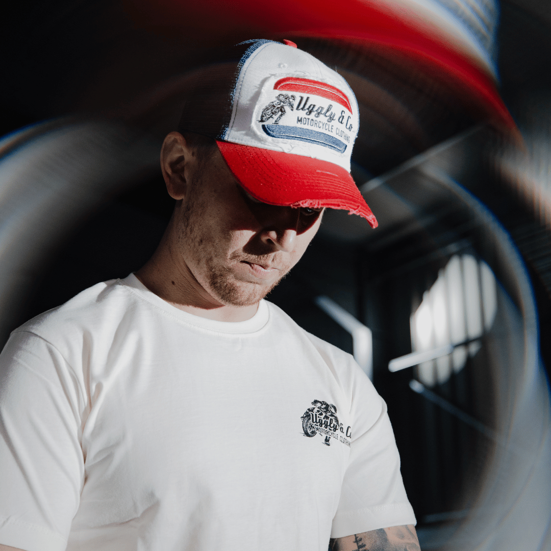 A model looking down while wearing a red, white and blue flat-track cap with a frayed Uggly&Co badge featuring a motorcycle racing theme