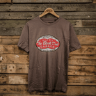 A gray crew neck t-shirt with 'The Black Dub Garage' text printed on the front, displayed against a wooden backdrop.
