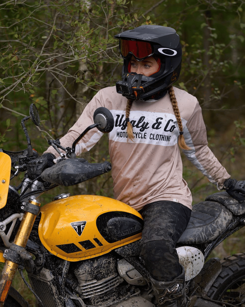 MX rider on a yellow motorcycle wearing a helmet and a branded MX shirt with a forest background