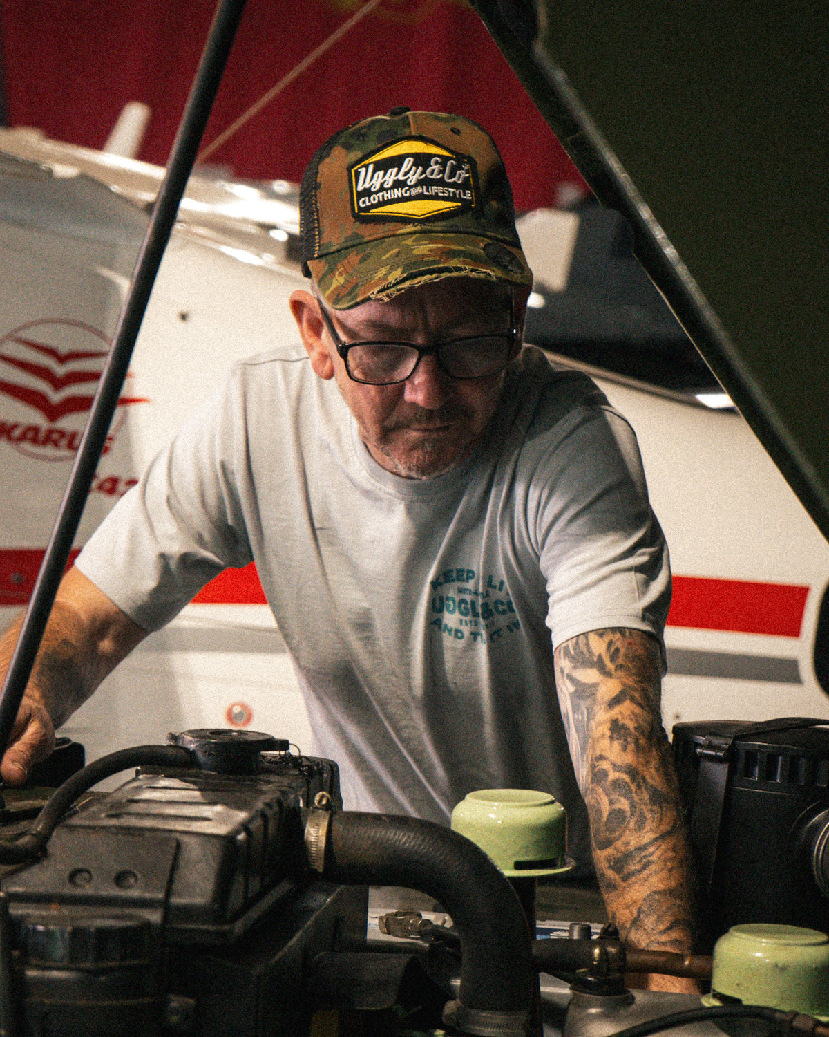 Man wearing a Green Camo Diamond Trucker Hat while working on a Land Rover in a workshop.