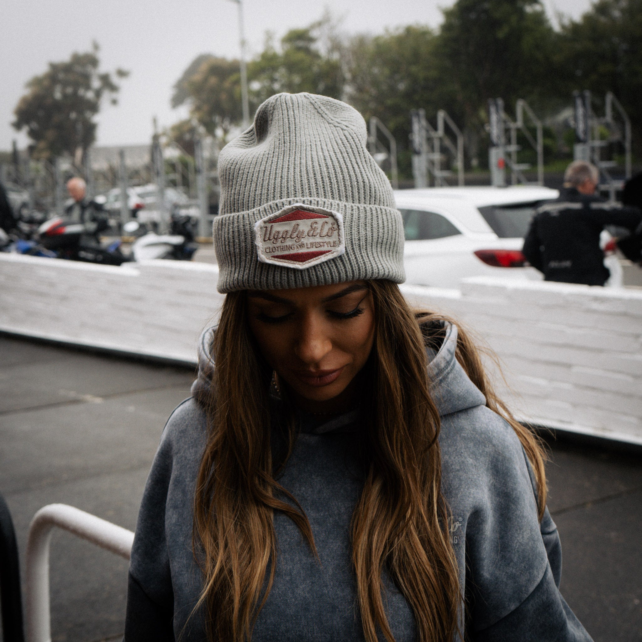 Female model wearing a grey beanie featuring the Uggly&Co Diamond logo trackside at the TT
