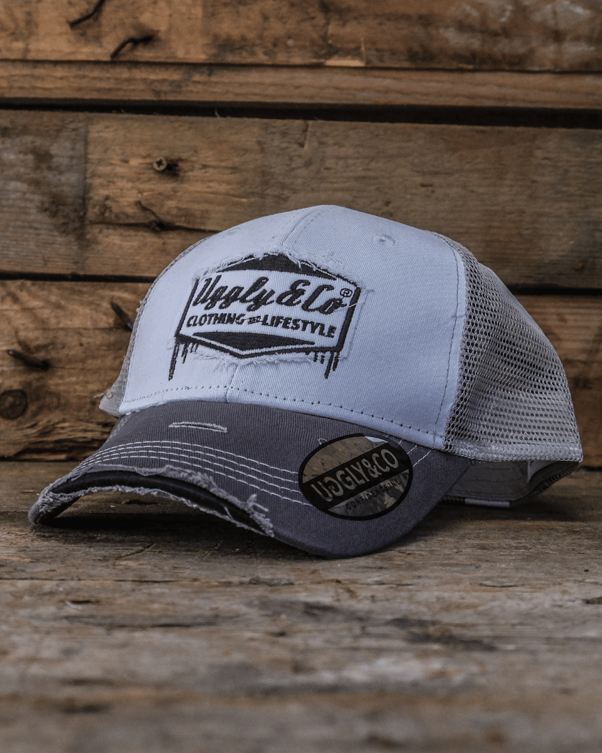 Grey and white trucker hat with an Uggly&Co logo on a wooden background