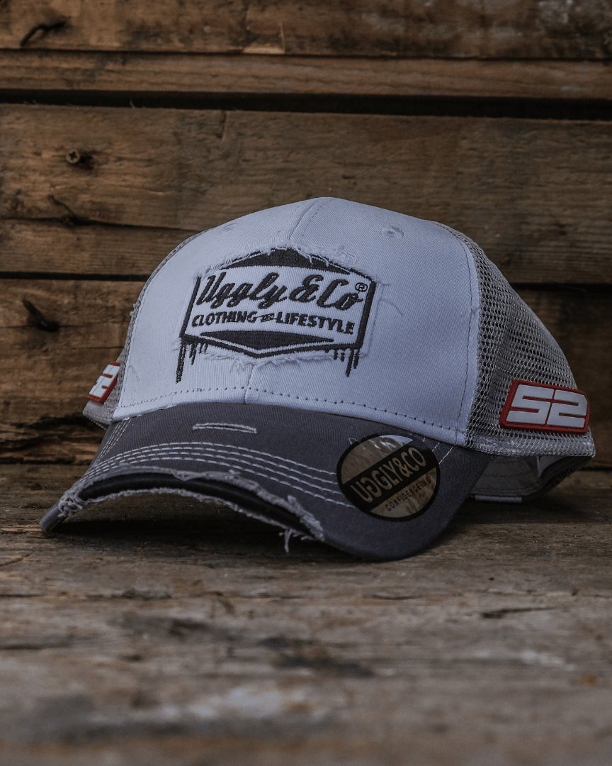 Grey and white trucker hat with Uggly&Co branding on a wooden background