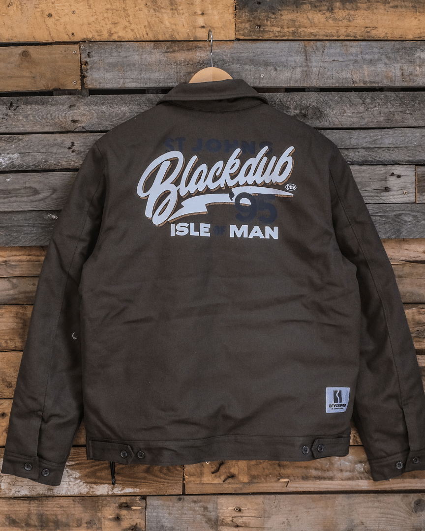 A green 'Since 95' Mechanic Jacket with a 'Black Dub Isle Man' graphic on the back, featuring a collar, branded rivets, and a heavy-duty industrial zipper.