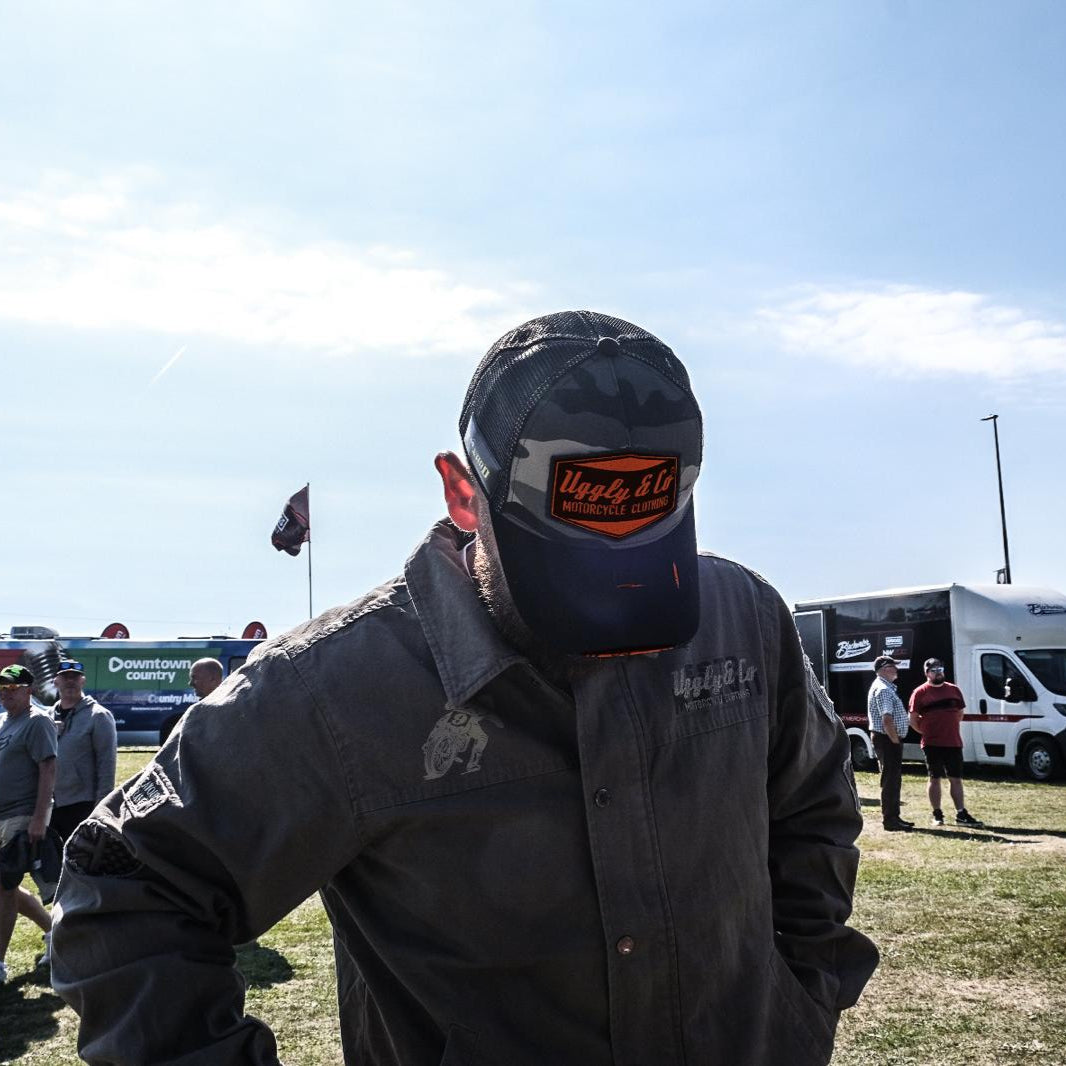 Person wearing a face mask with a visible brand logo in an outdoor setting with vehicles and people in the background.
