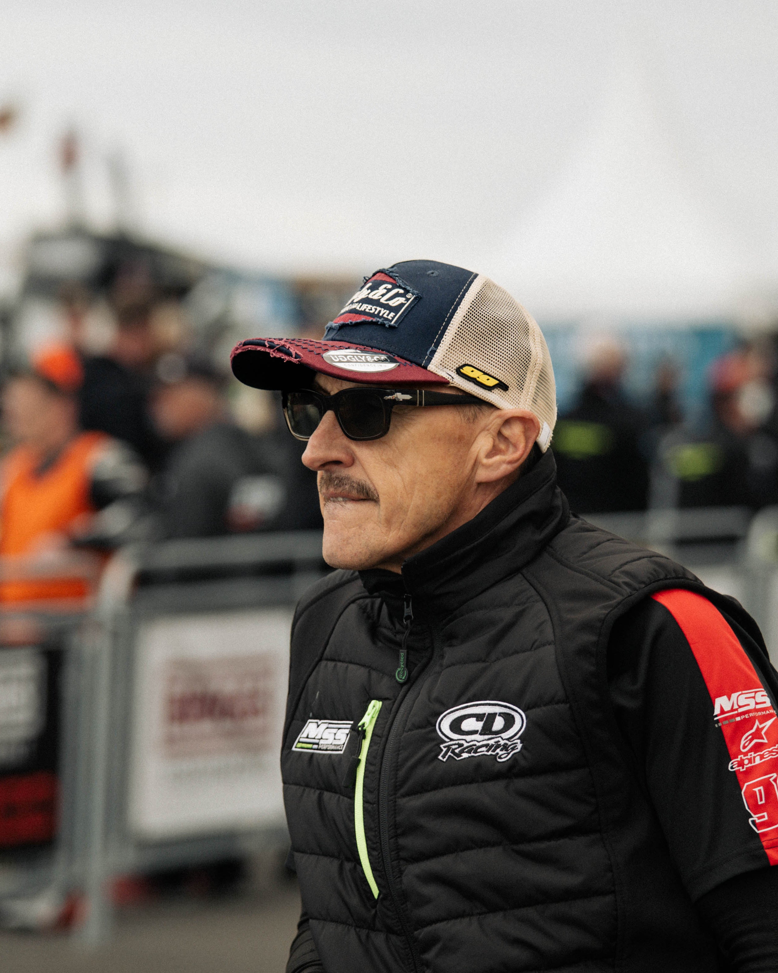 Jeremy McWilliams in the pit lane, stood wearing a hat and sunglasses on racetrack grid
