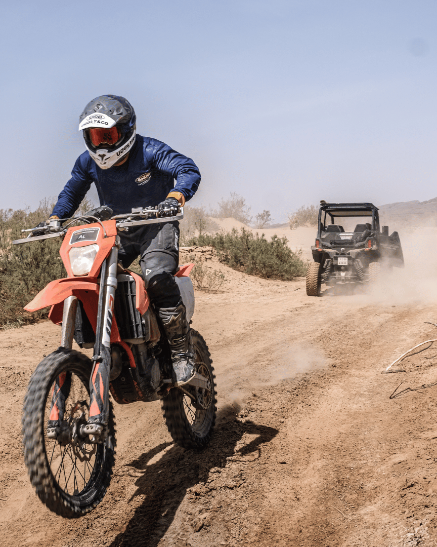 Riding a motocross bike down a desert trail in a blue motocross jersey and the brand name 'Uggly&Co Motorcycle Clothing' on the front