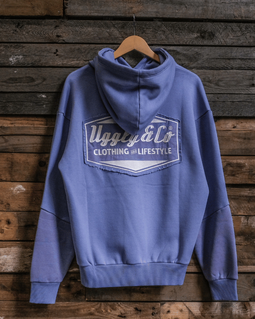 A purple surf diamond hoodie hanging on a wooden hanger against a wood panel background, with a white and pink logo on the back.