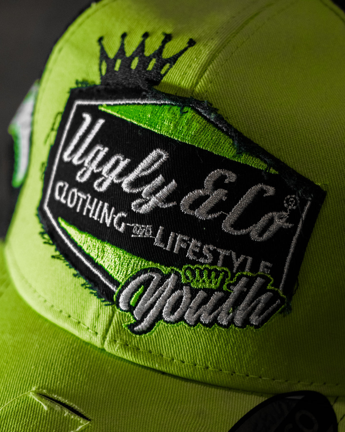 Close-up of the diamond logo on the Uggly & Co Fluro Diamond Trucker Hat x Kyle Ryde, photographed against a concrete floor.
