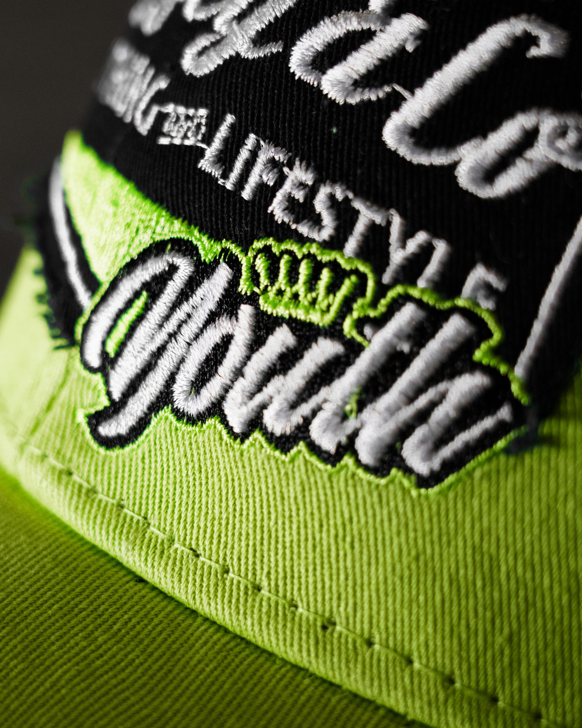 Close-up of the youth logo on the Uggly & Co Fluro Diamond Trucker Hat x Kyle Ryde, photographed against a concrete floor.