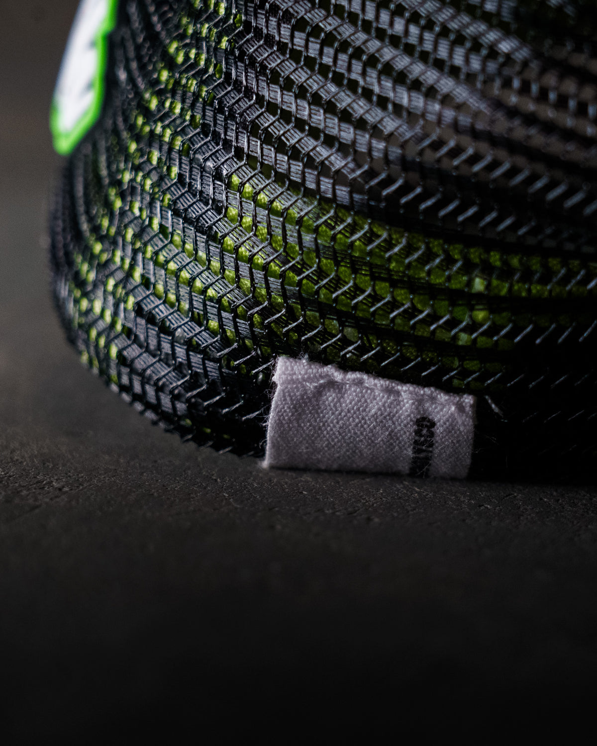 Close-up of the mesh panelling on the Uggly & Co Fluro Diamond Trucker Hat x Kyle Ryde, photographed on a concrete floor, highlighting the breathable trucker cap design.