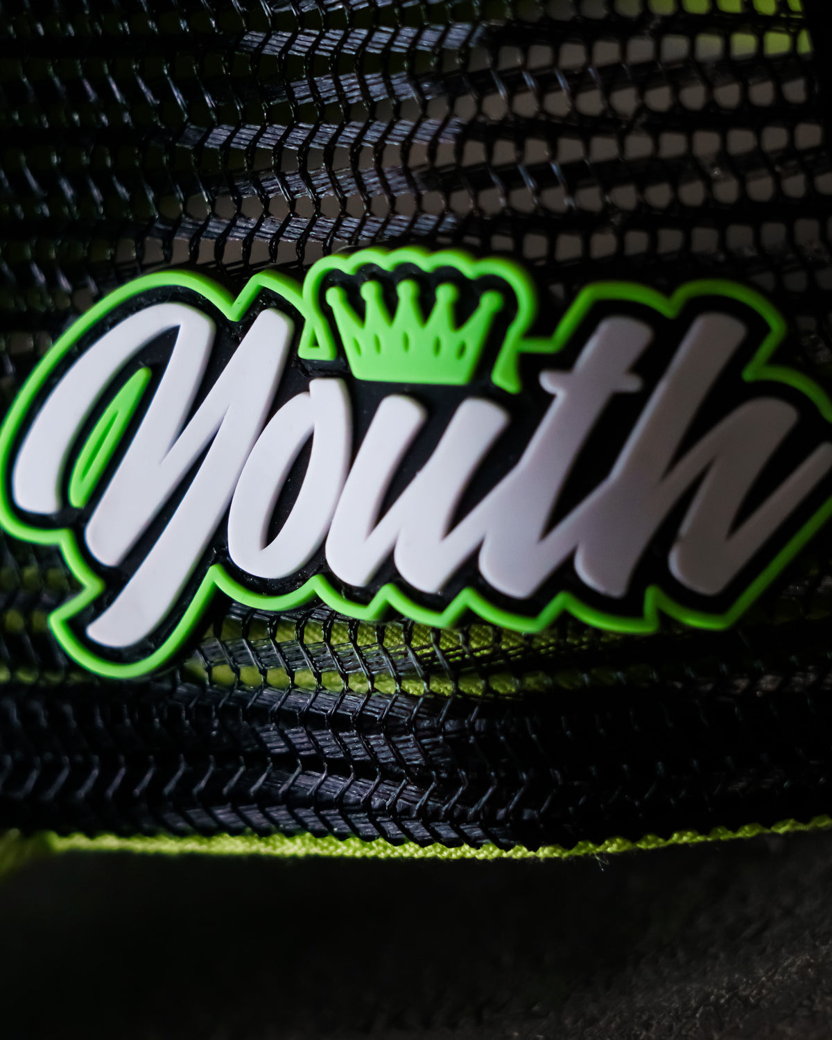 Close-up of the Youth badge on the Uggly & Co Fluro Diamond Trucker Hat x Kyle Ryde, photographed on a concrete floor, highlighting the badge detail on the British Superbikes inspired cap.