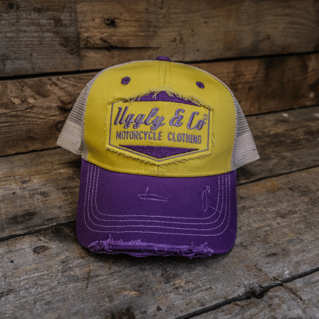 Front view of a yellow and purple trucker hat with a white mesh back, featuring the Uggly & Co Motorcycle Clothing logo on the front.