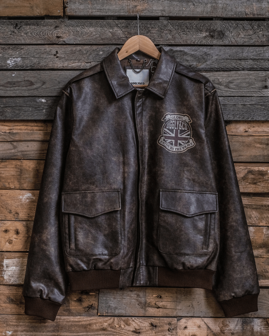 A brown leather aviation bomber jacket with a standing collar, displayed on a wooden hanger against a wooden background.