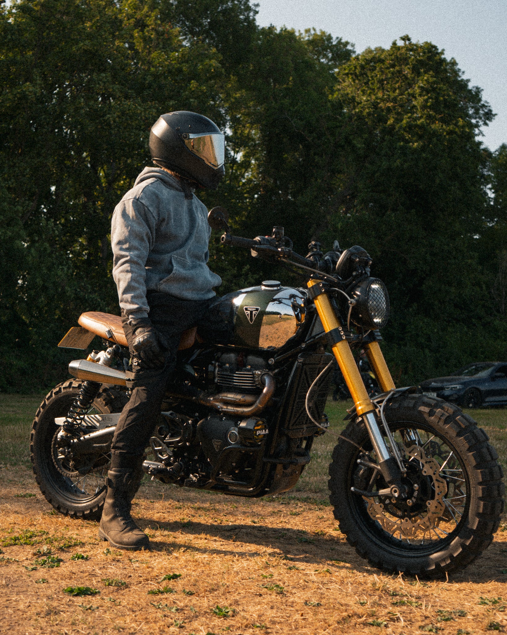 Man wearing an acid wash hoodie on a Triumph Scrambler motorcycle during a golden hour sunset.