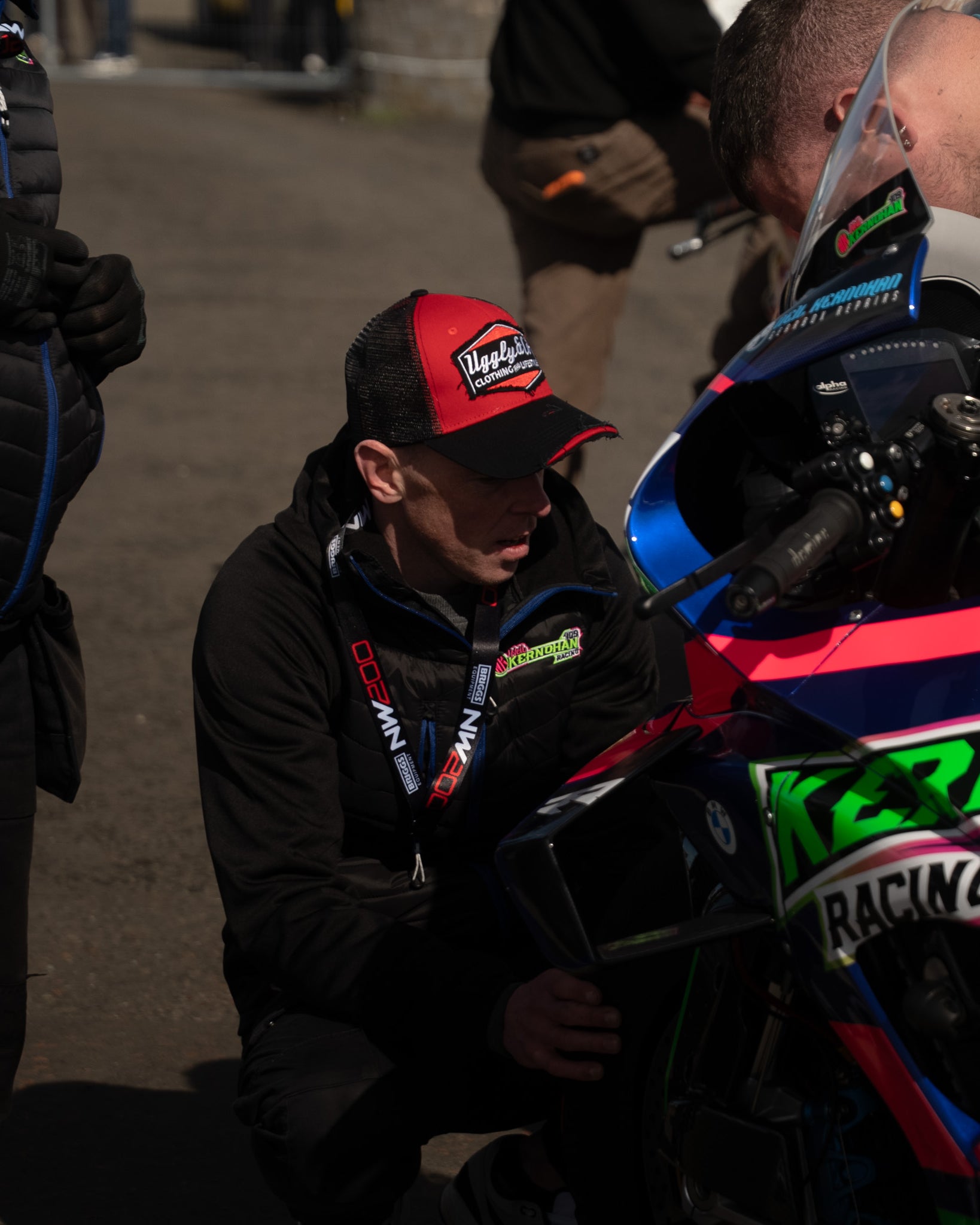 Man wearing black and red trucker hat working on a motorbike in a pit lane