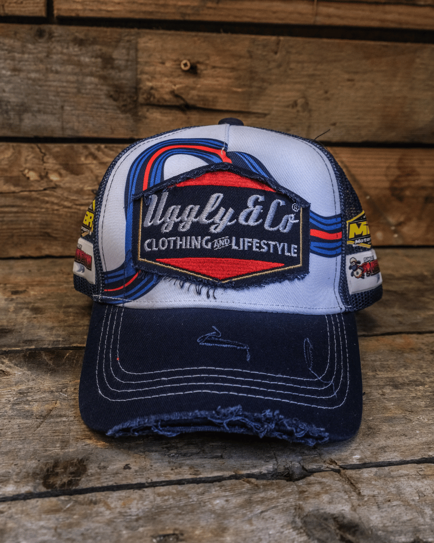 Front view of a white, red and blue trucker hat with a diamond Uggly&Co logo on a wooden background