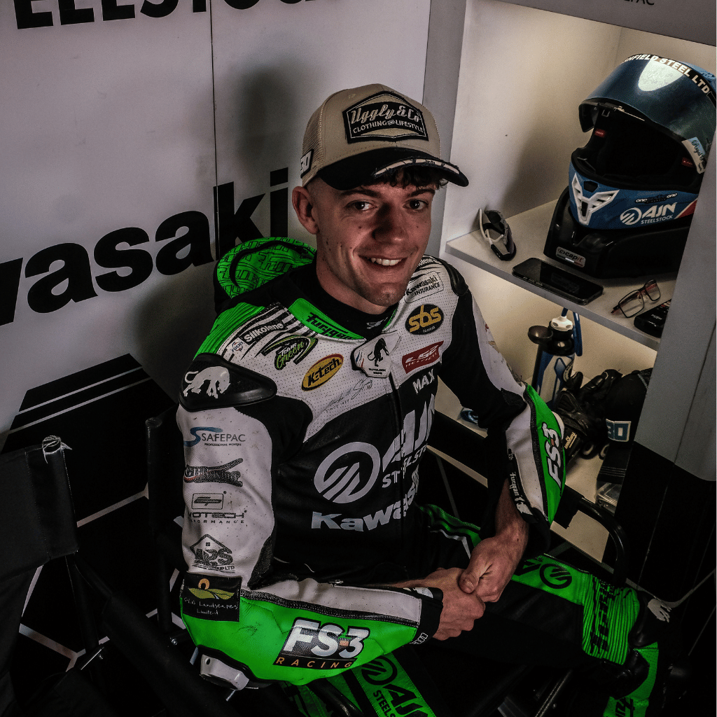 Max Cook in racing gear with Kawasaki branding in a garage setting and Uggly&Co trucker hat