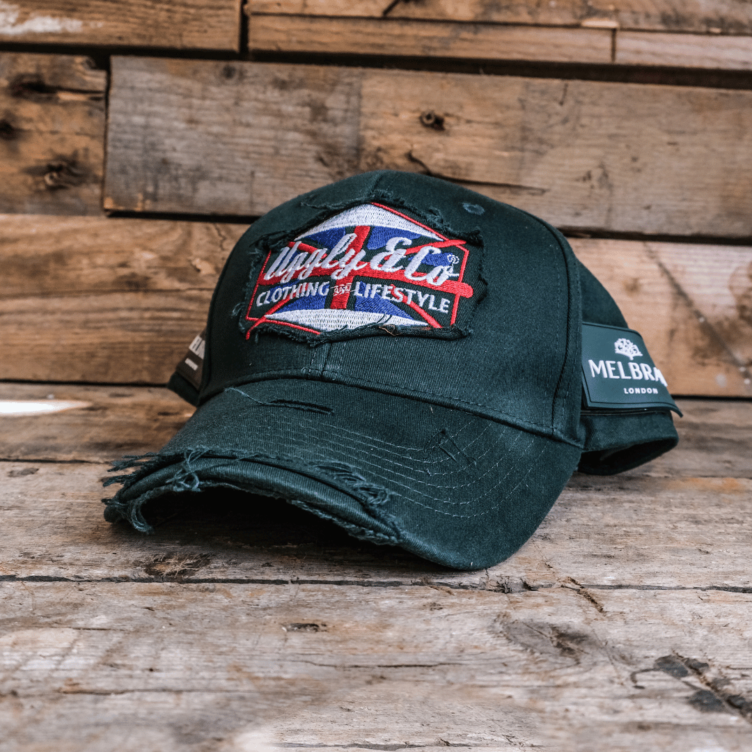 A green vintage cap with a union jack Uggly&Co brand logo on a wooden background
