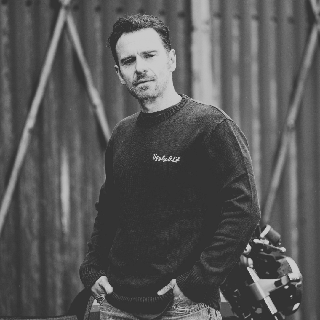 Man wearing a black sweater with text, holding a camera against a metallic background