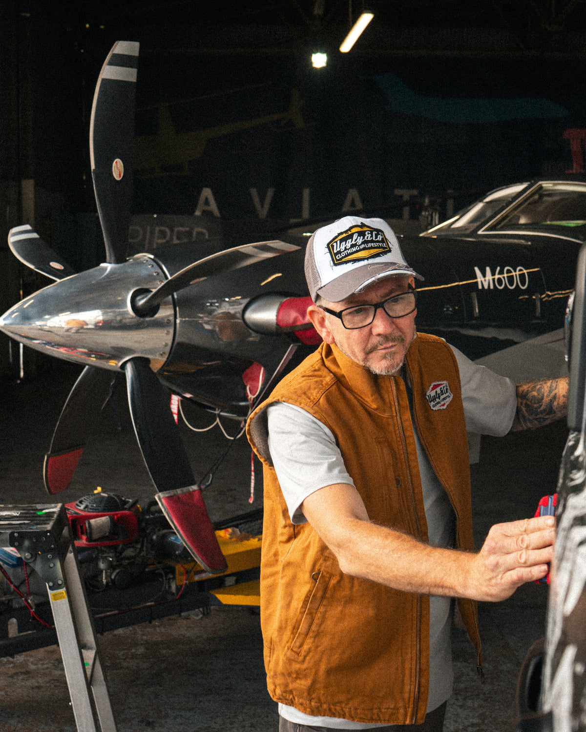 Mens Grey & White Diamond Trucker Cap worn inside an aircraft hangar during a vehicle wrap.