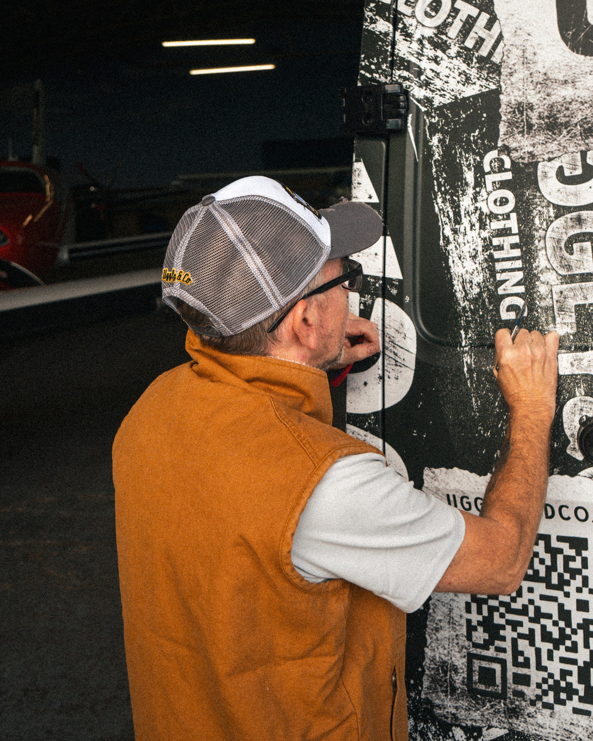 Grey and white vintage trucker cap worn by a man installing vinyl graphics on a van.