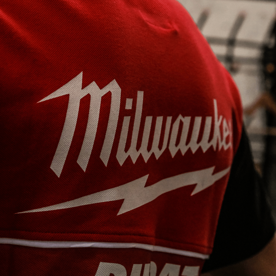 Close up of the Milwaukee logo on the back of a Milwaukee x Ducati polo shirt, featuring a black lower half and a red upper torso