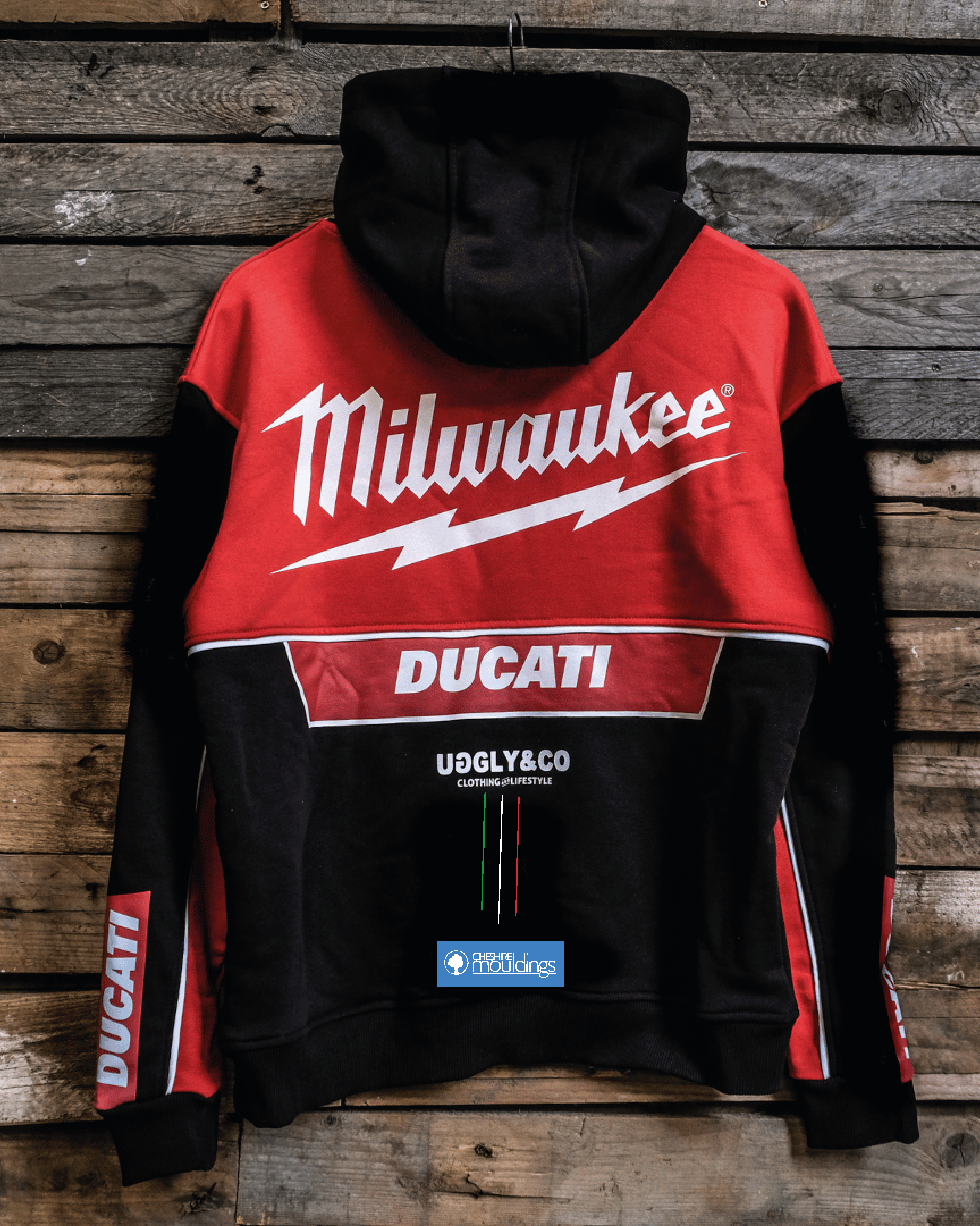 A Milwaukee Tools x DUCATI teamwear hoodie with red and black color scheme, featuring the DUCATI logo and official 2025 Uggly&Co collaboration branding, displayed on a wooden background.