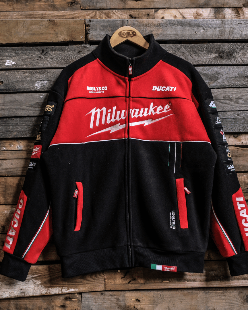 A Milwaukee Tools x DUCATI official merchandise track jacket displayed on a wooden backdrop, featuring a black and red color scheme with branding and logos.