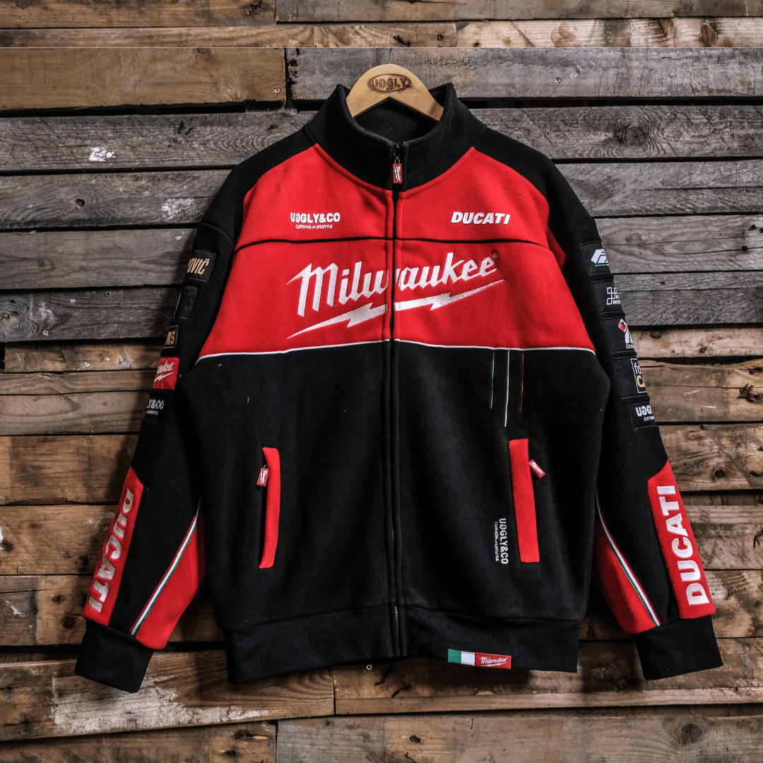 A Milwaukee Tools x DUCATI official merchandise track jacket displayed on a wooden backdrop, featuring a black and red color scheme with branding and logos.