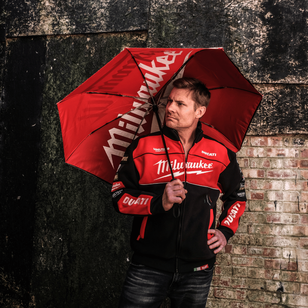 A model looking left and holding a Milwaukee Tools x Ducati umbrella with a black canopy and red accents, featuring the Milwaukee Tools logo, Ducati logo, and the Uggly&Co logo