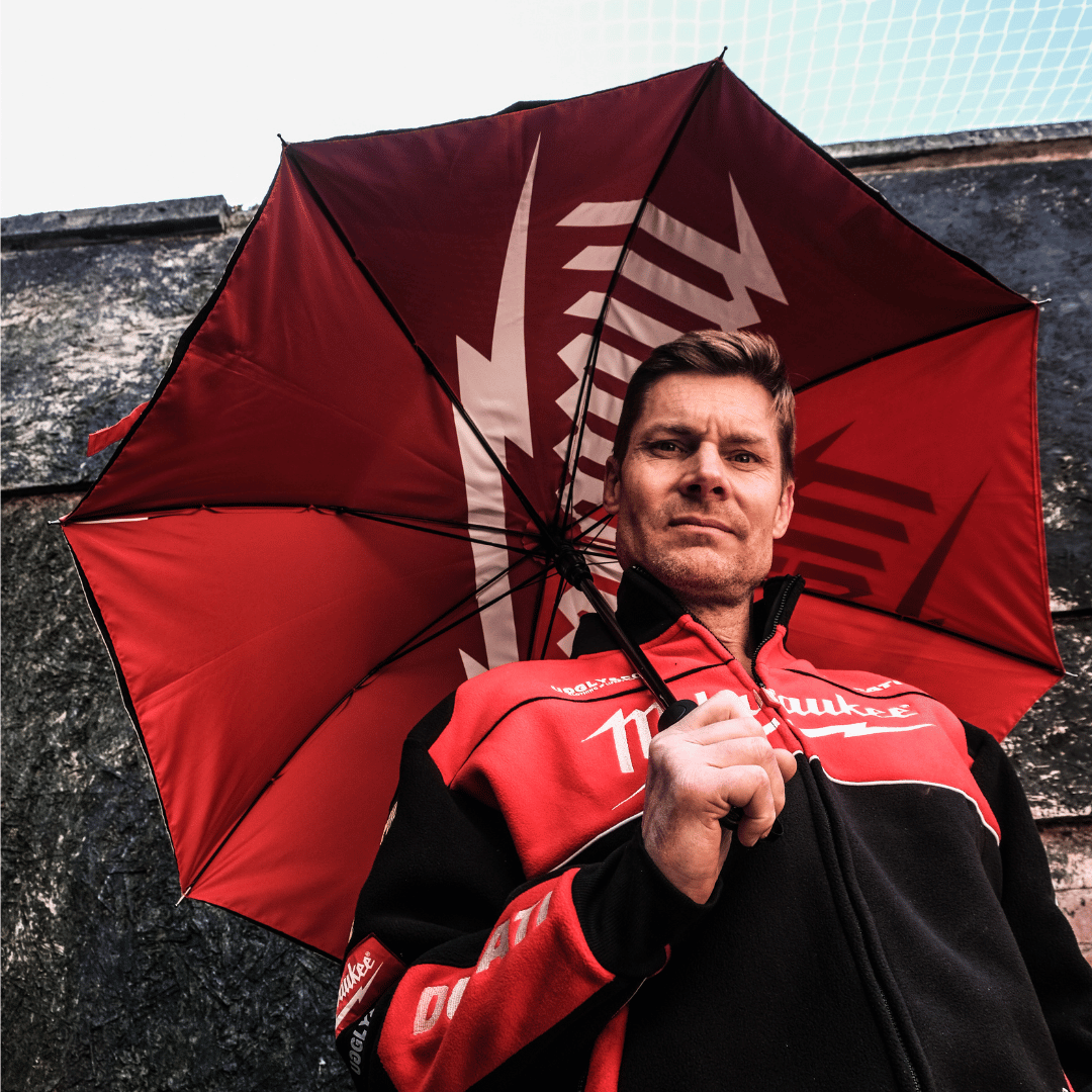 A model looking down at the camera and holding a red and black Milwaukee x Ducati umbrella with Milwaukee logo against a brick wall backdrop
