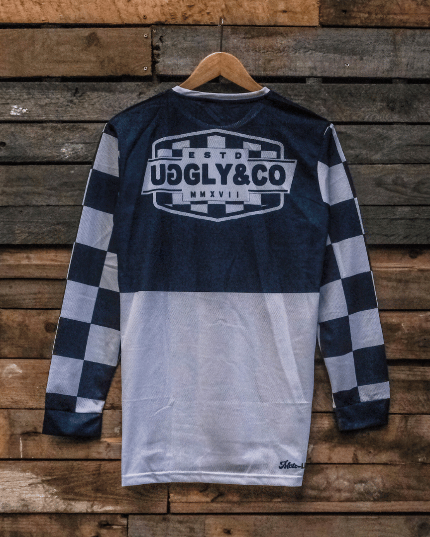 Backwards facing checkered long-sleeve MX shirt with an Uggly&Co brand logo on a wooden background