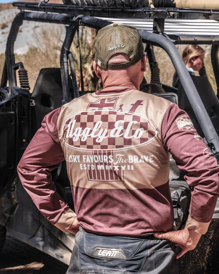 A motocross rider standing in the desert in a brown Uggly&Co MX shirt, rear view