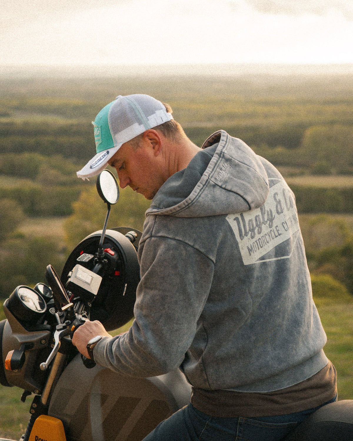 Motorcyclist in a turquoise and white trucker hat with a Royal Enfield Scram 411 scrambler