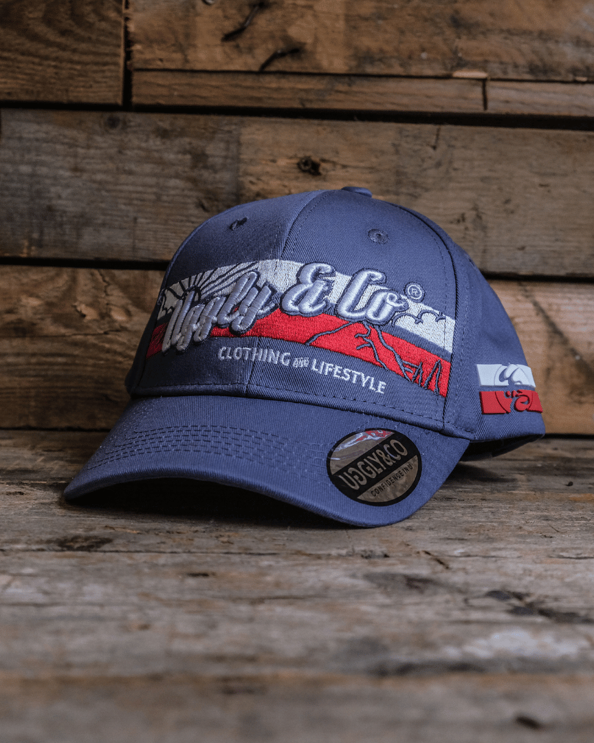 A royal blue Uggly&Co vintage cap with a white and red design on the front, displayed on a wooden surface.