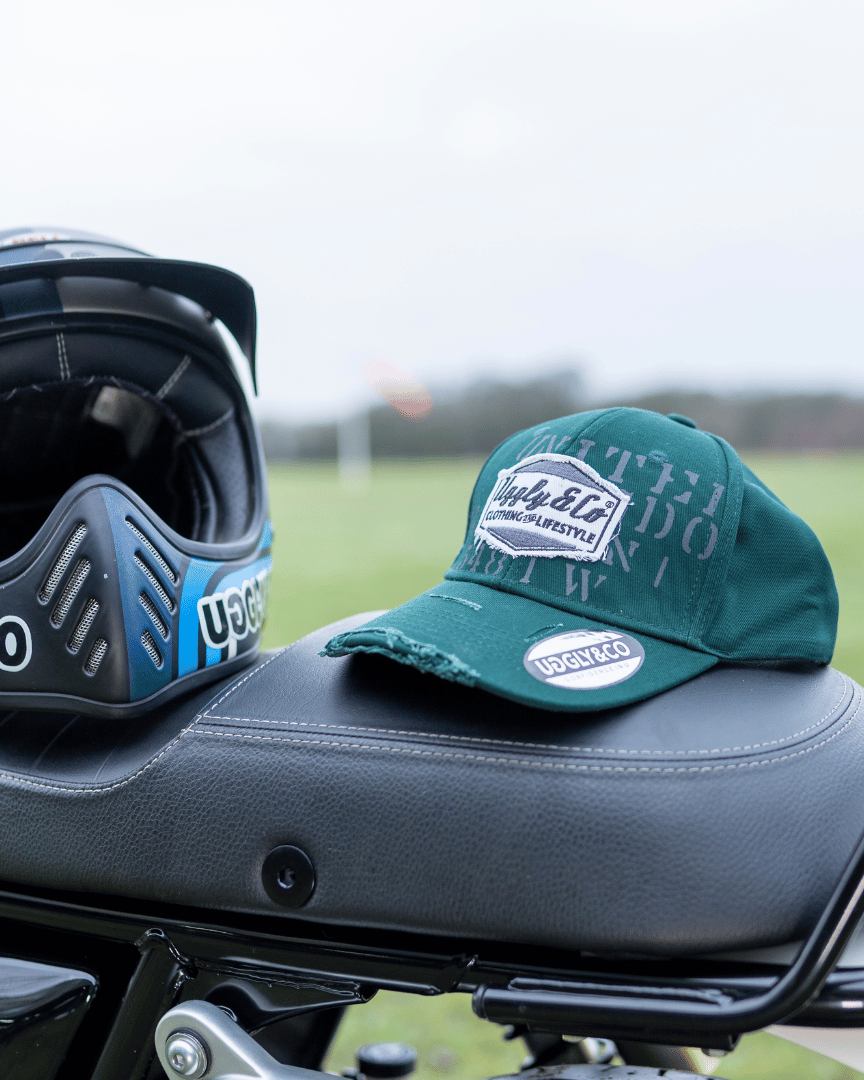 A green 'Aviation' Diamond Trucker Hat with distressed black and white Uggly&Co logo placed on a motorcycle seat on an airfield