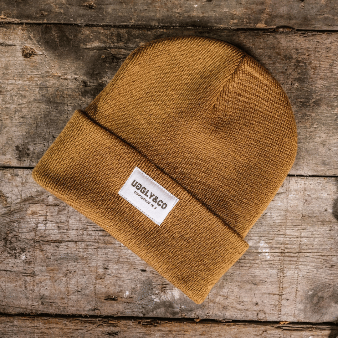 A mustard yellow 'fisherman' beanie with the UGGLY&CO brand label visible on the cuff.