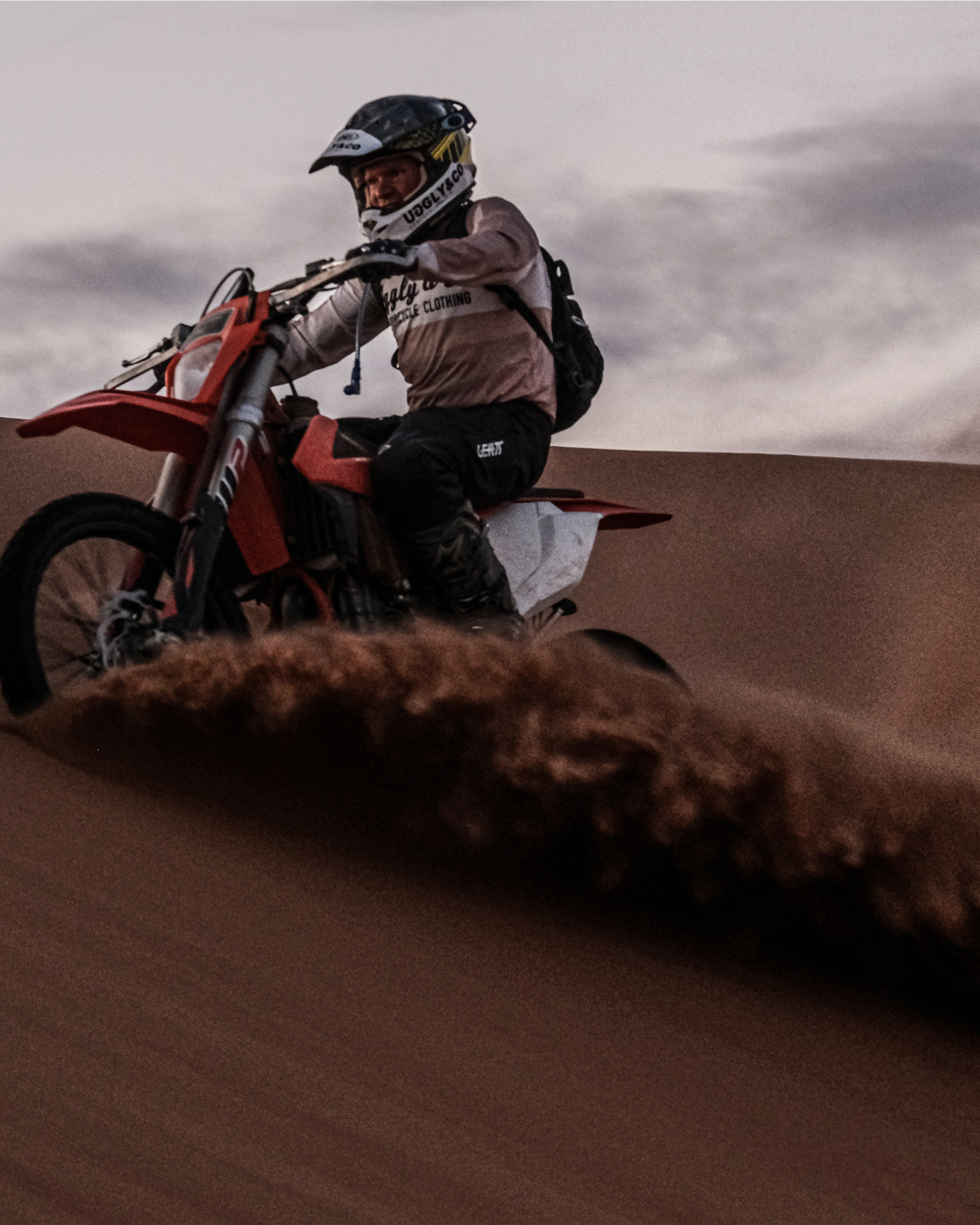 MX rider on sand dunes in a long-sleeve motocross jersey with 'Uggly & Co Motorcycle Clothing' logo