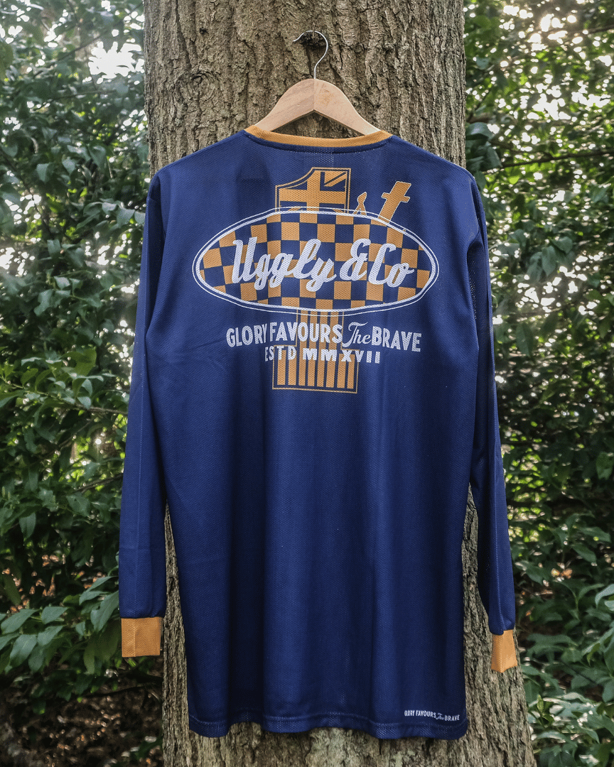 A blue and yellow long-sleeved motocross jersey hanging on a tree backwards with graphical designs and text on the back.