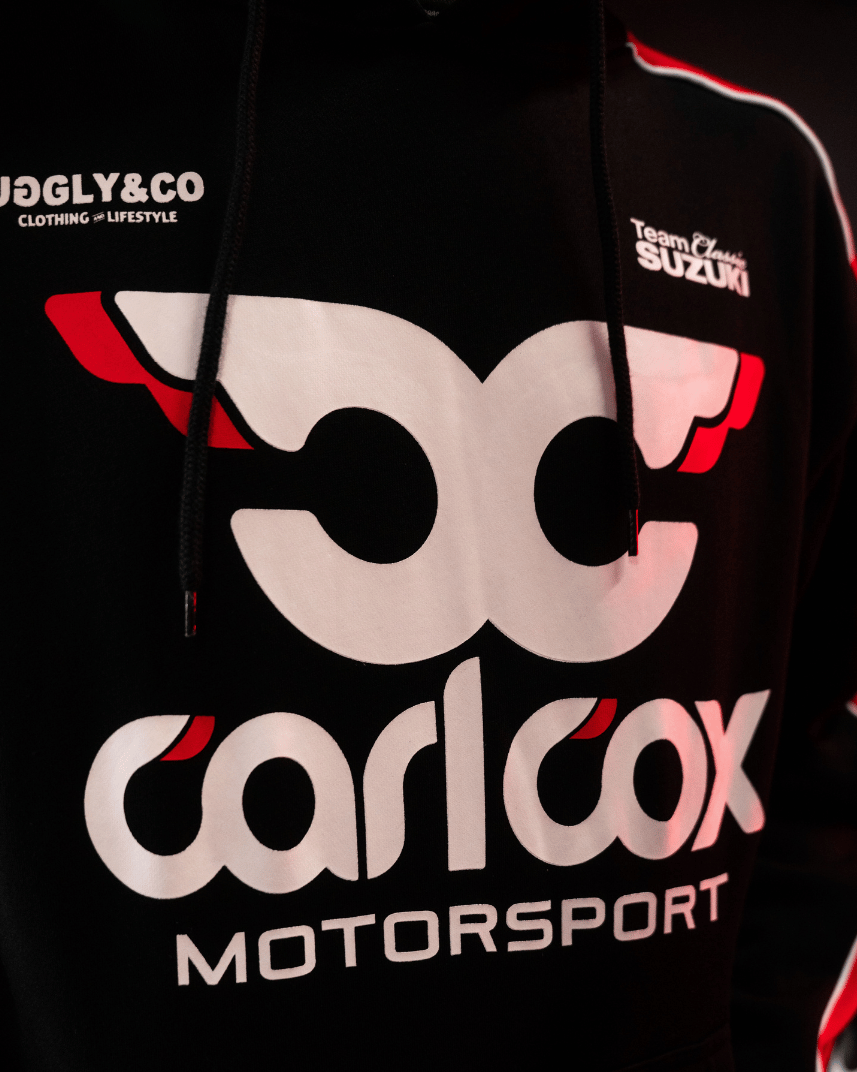 Close up of the front detailing on a black hoodie with red sleeves featuring Carl Cox Motorsport, Team Classic Suzuki and Uggly&Co branding