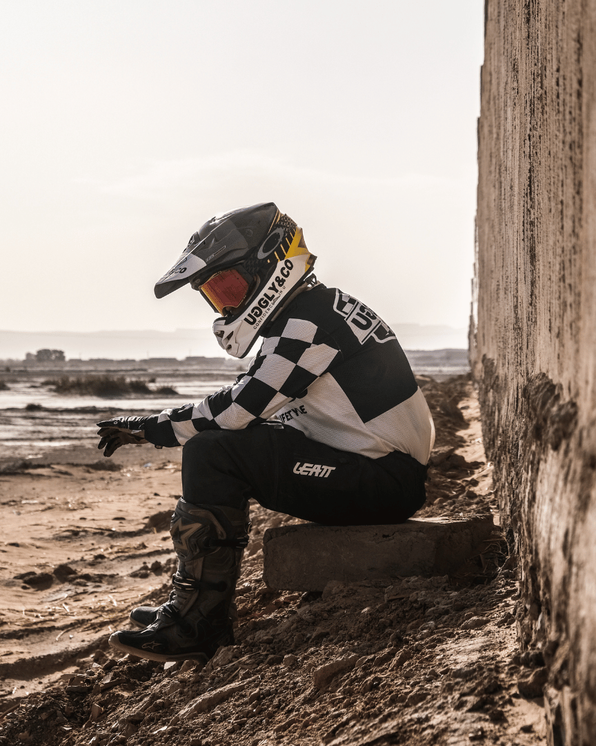 Motocross rider in full gear sitting in the desert wearing a chequered Uggly&Co MX shirt