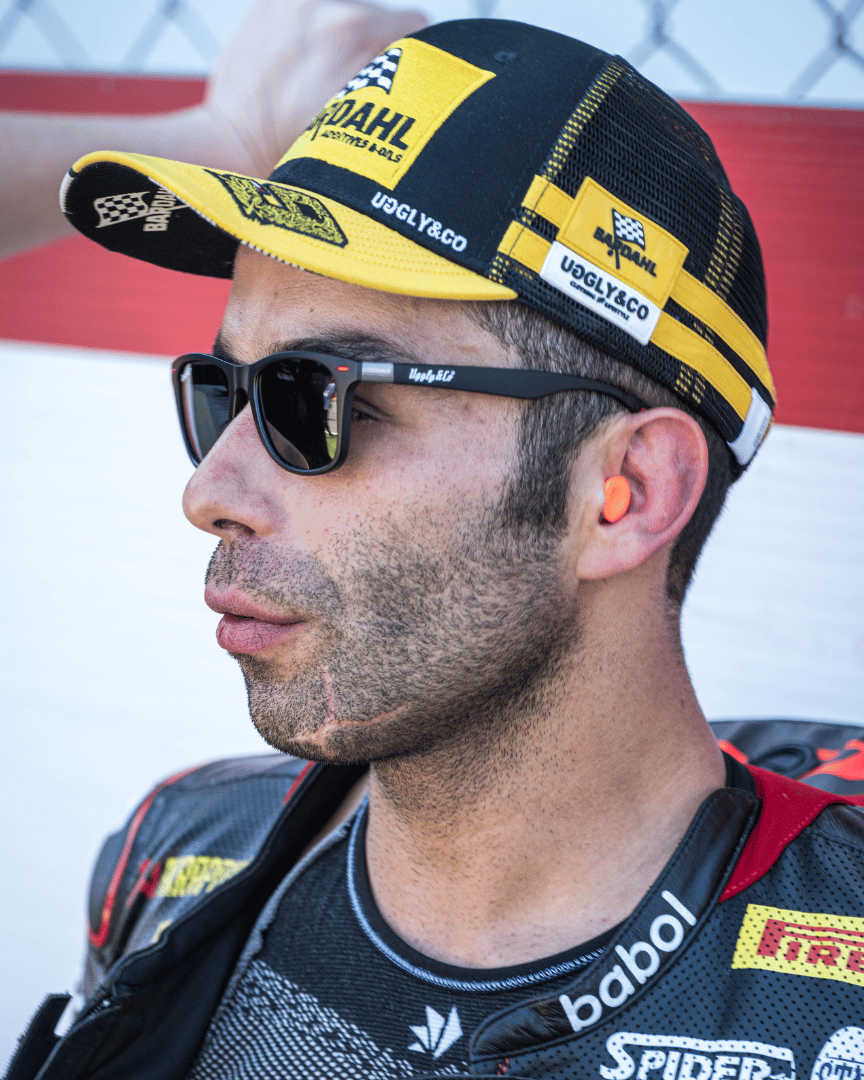 Danilo Pertrucci looking left while wearing a yellow and black Uggly&Co Bardahl Danilo Pertrucci #9 merchandise trucker hat