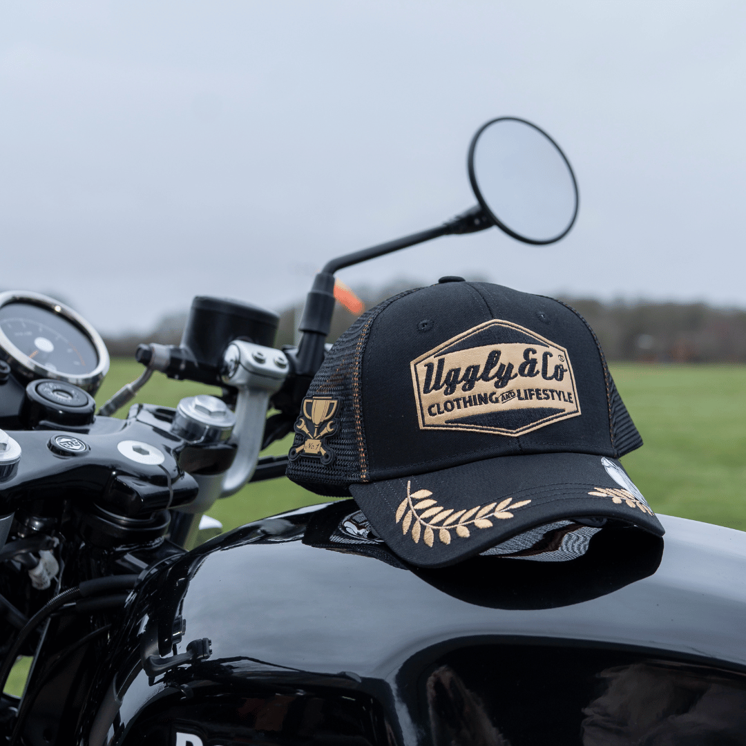 Black trucker hat with a gold Uggly&Co logo on a motorcycle