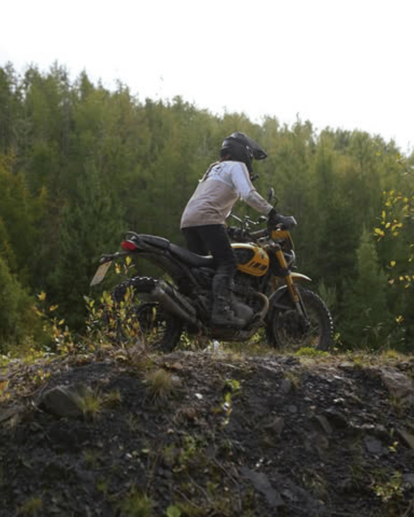 Person riding a motorcycle on a rocky trail with trees in the background