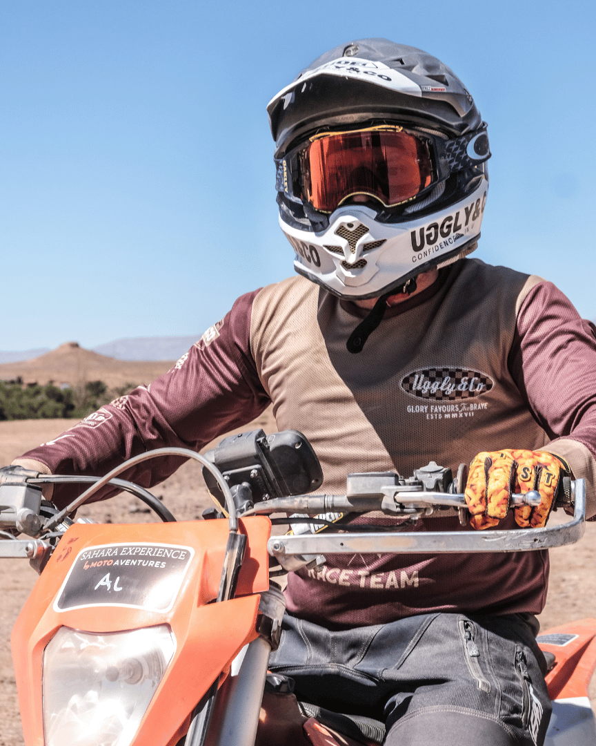 A person on an MX bike in a long-sleeved brown and beige motocross jersey in the desert