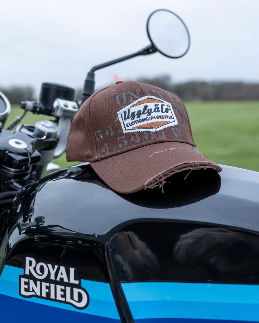 A brown 'Aviation' Diamond Trucker Hat with the Uggly&Co logo on the front resting on a motorcycle fuel tank