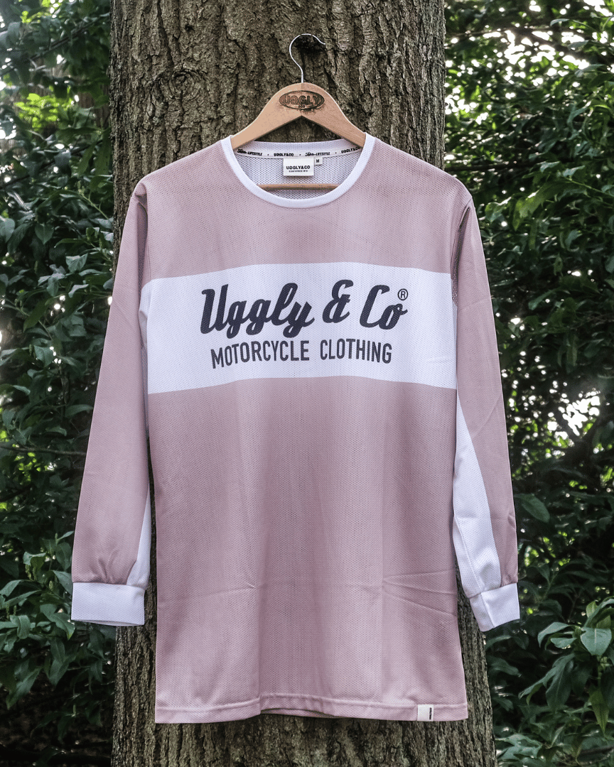 A beige motocross jersey with a diamond logo and the brand name 'Uggly&Co Motorcycle Clothing' on the front and back, hanging on a tree, front view